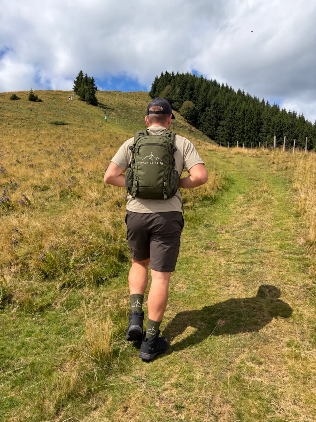 Einer der WALK BY FAITH Gründer auf einem Bergweg, mit digital bearbeiteter Markenkleidung